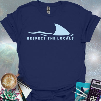 A blue shark fin rising above blue ocean waves, with the text 'RESPECT THE LOCALS' below.