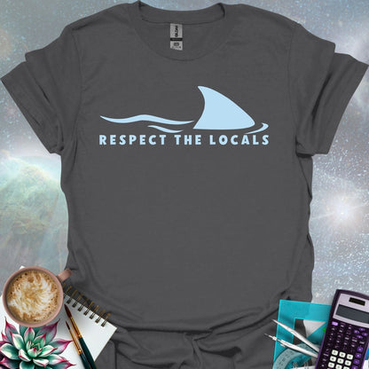A blue shark fin rising above blue ocean waves, with the text 'RESPECT THE LOCALS' below.