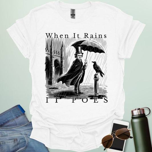 A literary pun t-shirt with a vintage illustration of Edgar Allan Poe holding an umbrella in the rain, next to a raven. The text reads 'When It Rains It Poes.'