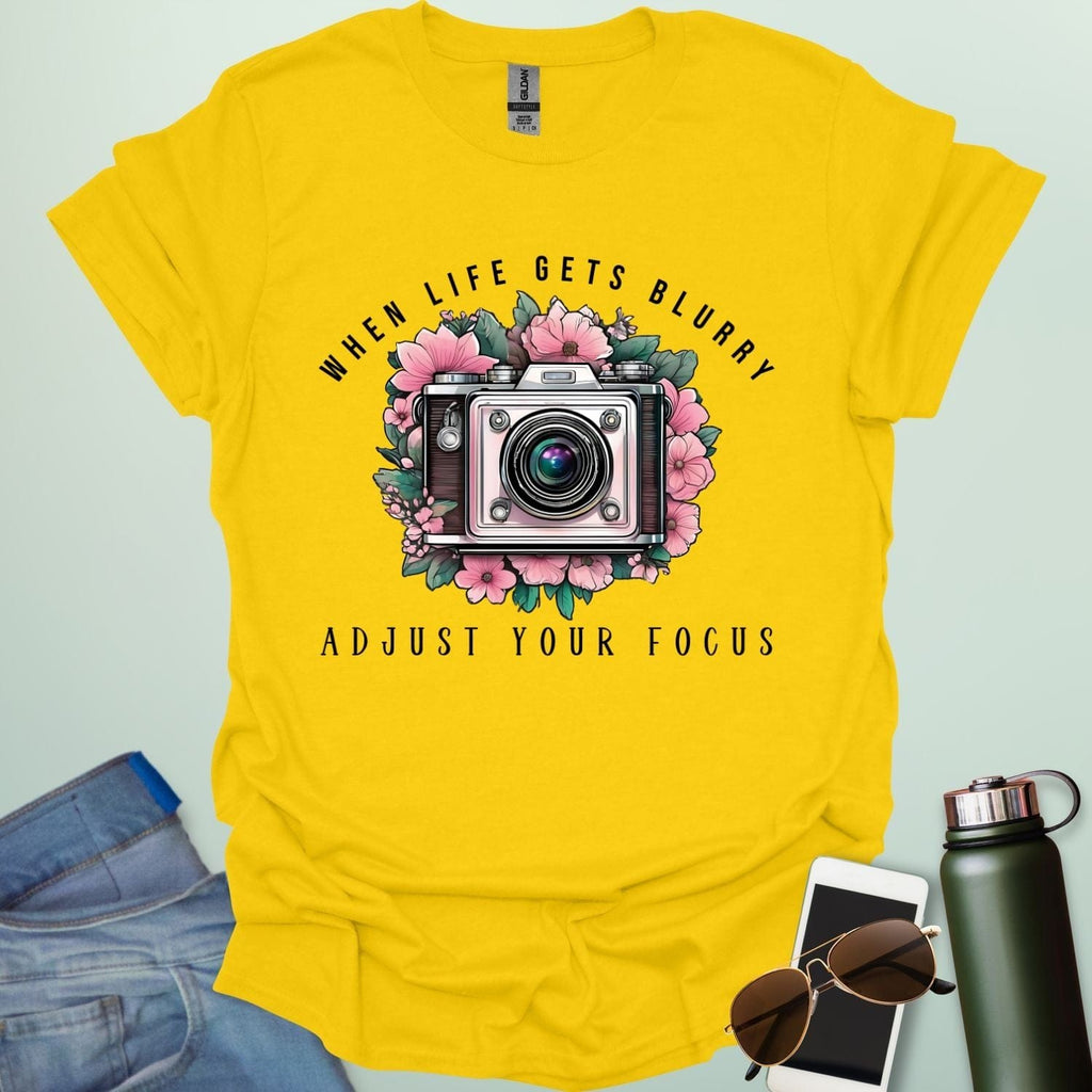 Vintage camera surrounded by flowers with the quote “When Life Gets Blurry, Adjust Your Focus.”
