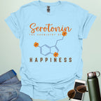 The word 'Serotonin' in cursive orange font above the text 'THE CHEMISTRY OF' in smaller orange font, above the chemical structure of serotonin in light blue with three orange flowers incorporated into the bonds. Below the chemical structure is the word 'HAPPINESS' in bold orange font.