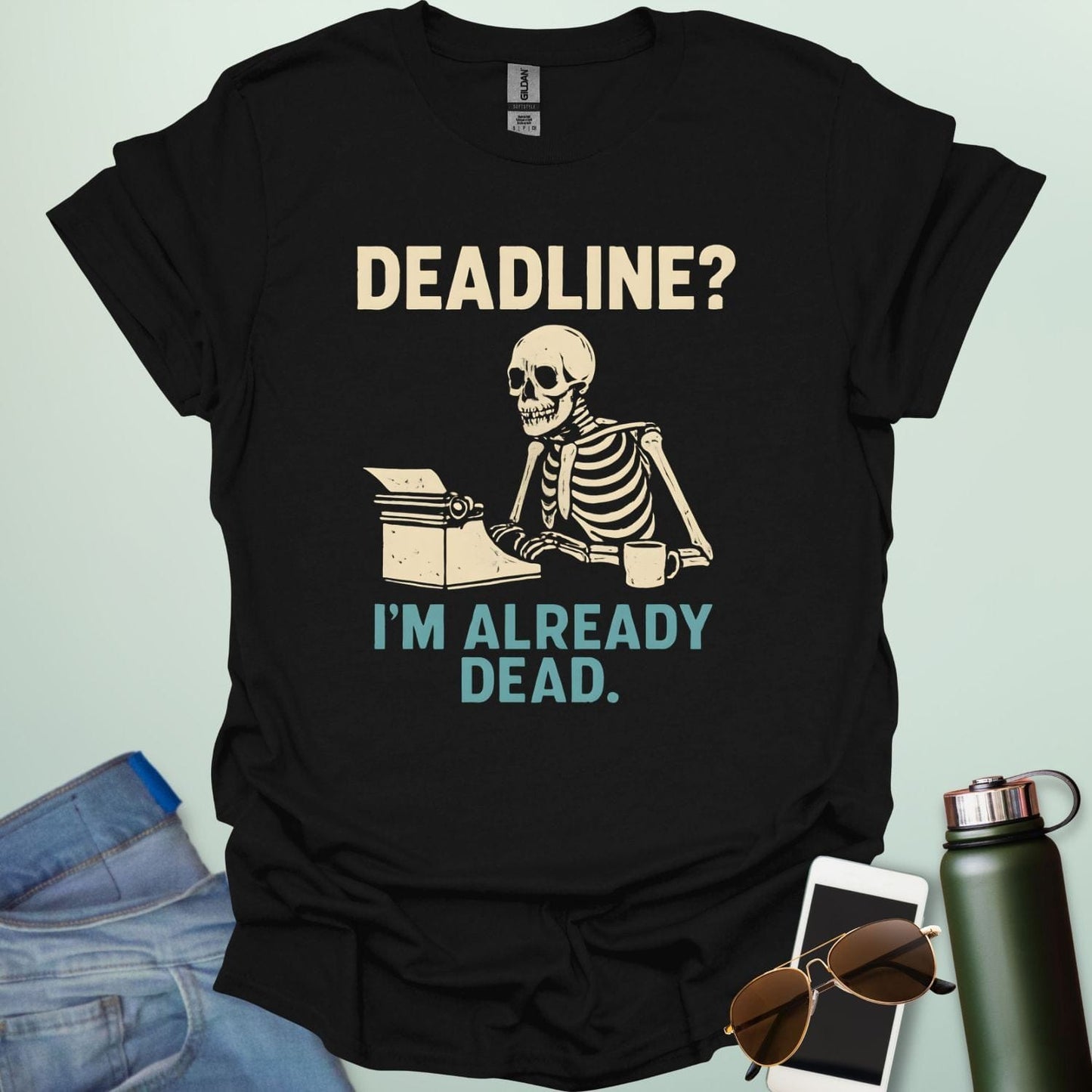 A vintage-style graphic featuring a skeleton sitting at a desk with a coffee mug, typing on a typewriter between the text "DEADLINE? I'M ALREADY DEAD."