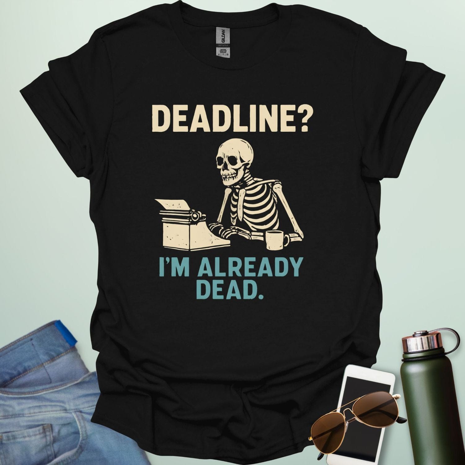 A vintage-style graphic featuring a skeleton sitting at a desk with a coffee mug, typing on a typewriter between the text "DEADLINE? I'M ALREADY DEAD."