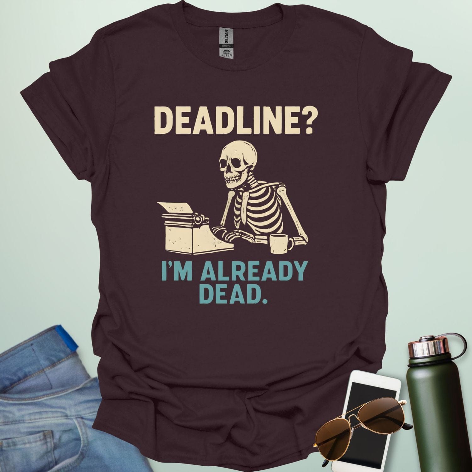 A vintage-style graphic featuring a skeleton sitting at a desk with a coffee mug, typing on a typewriter between the text "DEADLINE? I'M ALREADY DEAD."