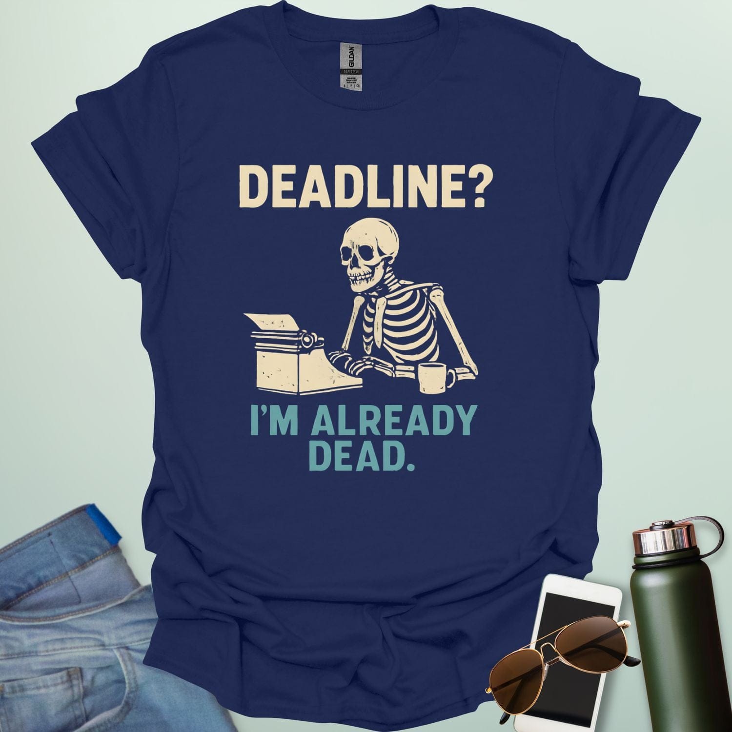 A vintage-style graphic featuring a skeleton sitting at a desk with a coffee mug, typing on a typewriter between the text "DEADLINE? I'M ALREADY DEAD."