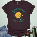 A cheerful graphic design featuring a smiling yellow proton character with orbiting electrons and the text "BE LIKE A PROTON STAY POSITIVE."