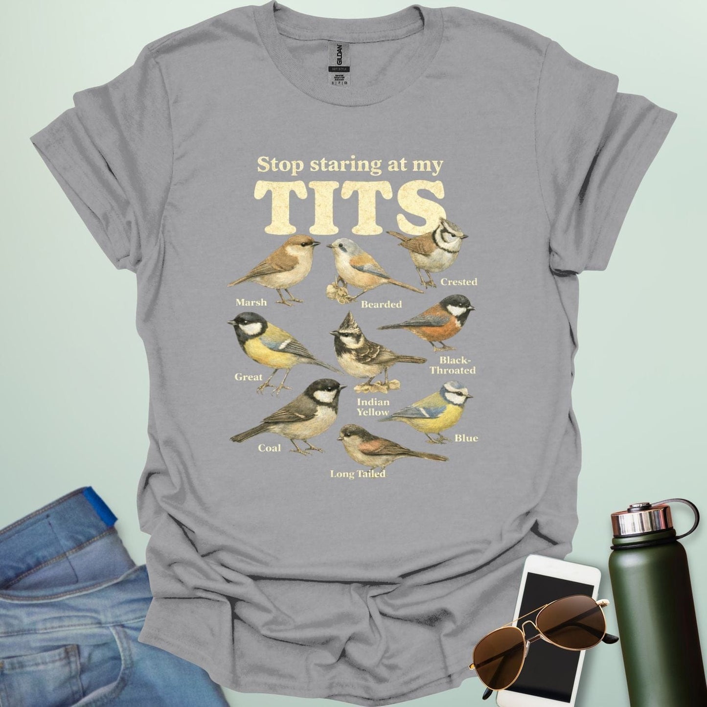 A t-shirt featuring the text "Stop staring at my TITS" above nine vintage-style illustrations of different tit bird species, including the Bearded, Crested, and Long Tailed tits.