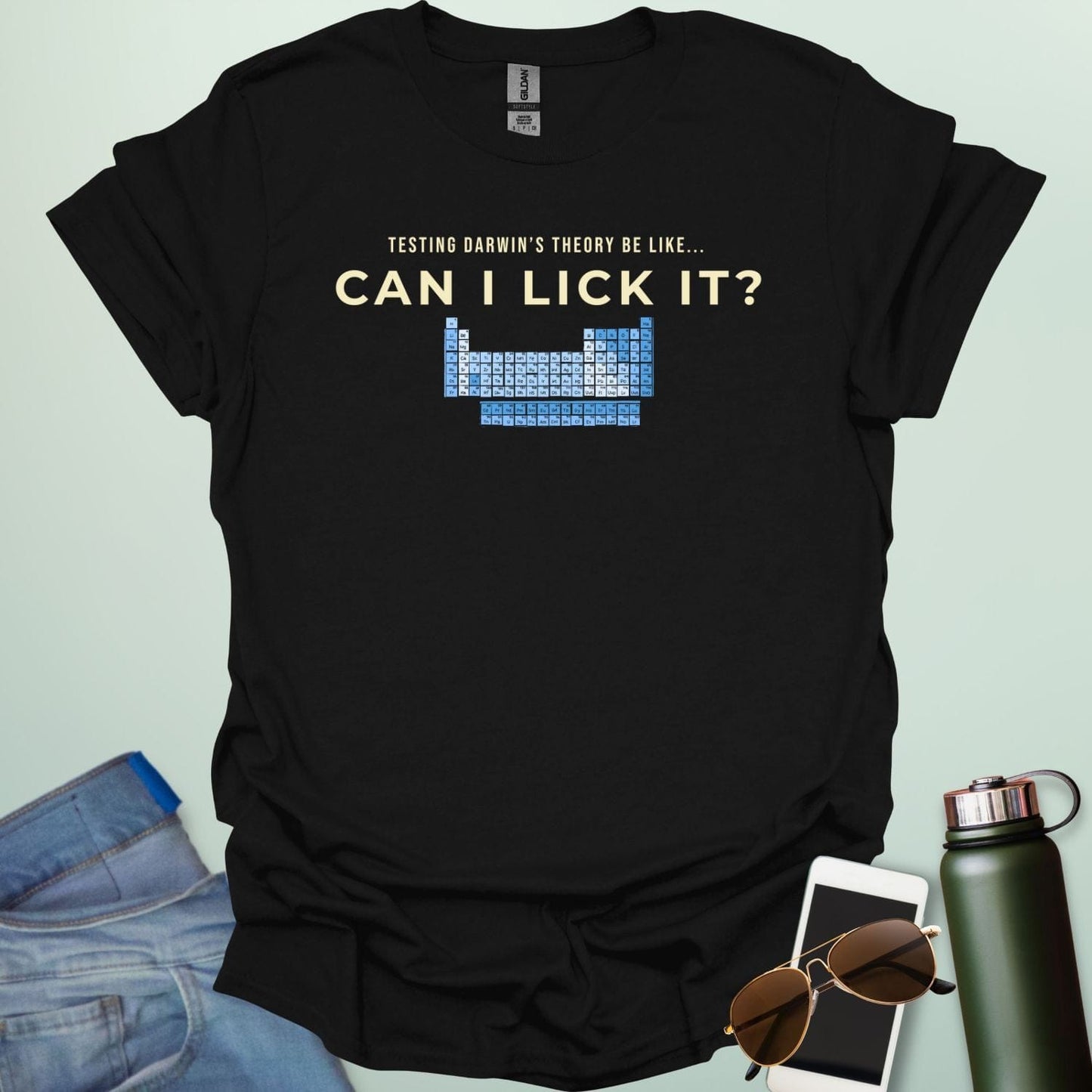 A graphic design featuring the text "TESTING DARWIN'S THEORY BE LIKE..." above the large question "CAN I LICK IT?" and a blue-toned periodic table of elements.
