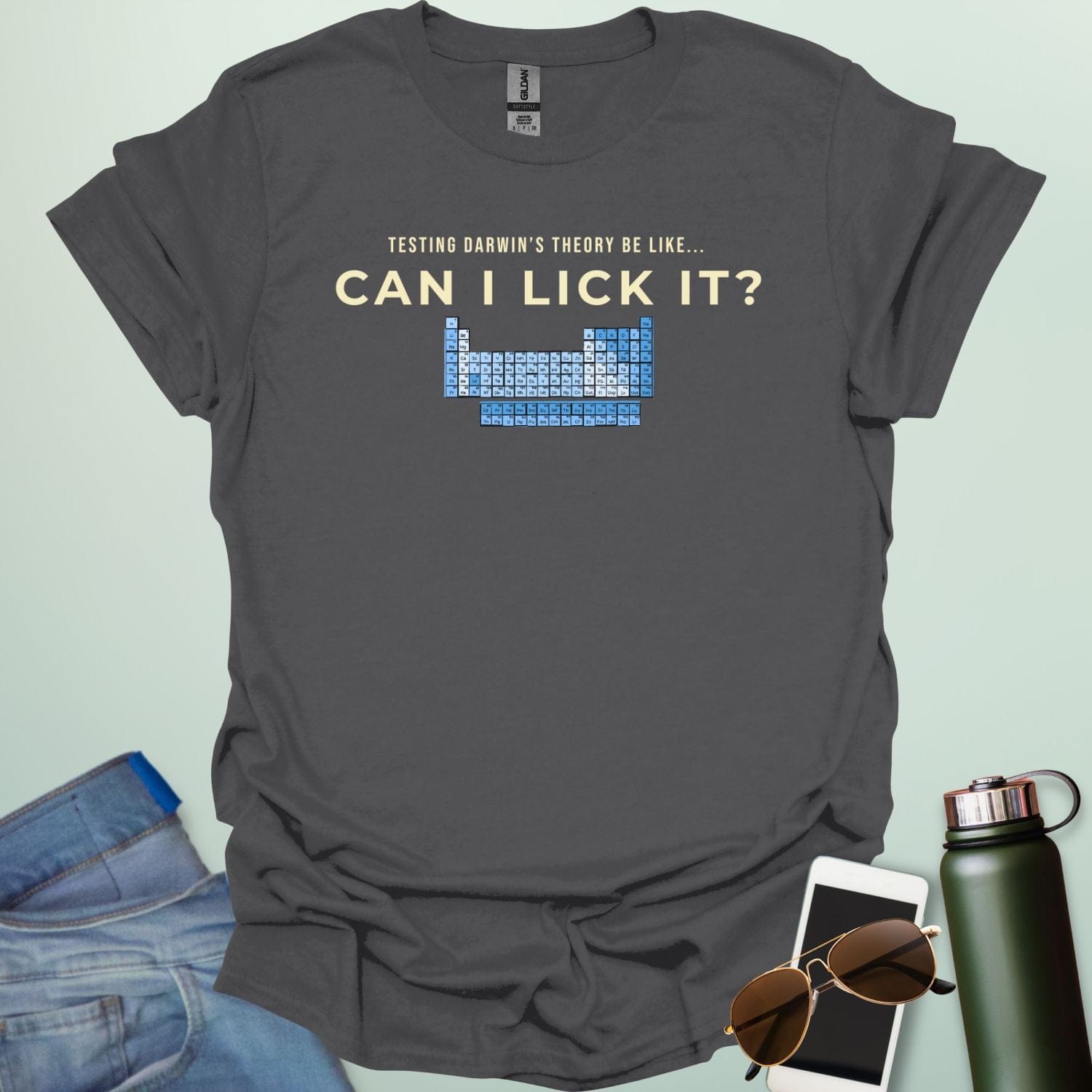 A graphic design featuring the text "TESTING DARWIN'S THEORY BE LIKE..." above the large question "CAN I LICK IT?" and a blue-toned periodic table of elements.