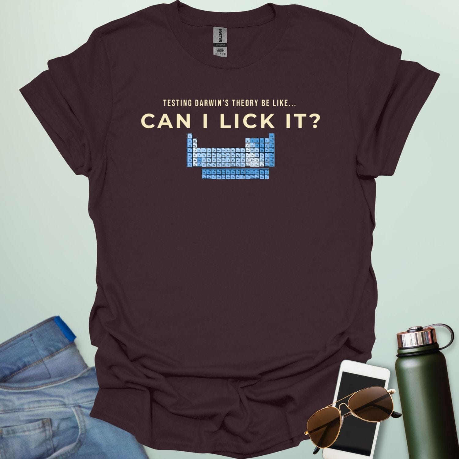 A graphic design featuring the text "TESTING DARWIN'S THEORY BE LIKE..." above the large question "CAN I LICK IT?" and a blue-toned periodic table of elements.