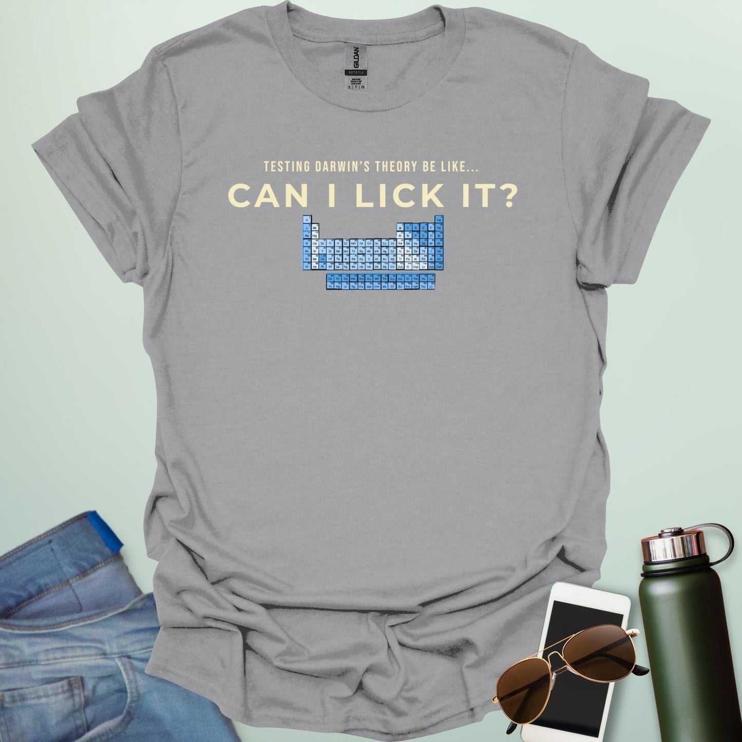 A graphic design featuring the text "TESTING DARWIN'S THEORY BE LIKE..." above the large question "CAN I LICK IT?" and a blue-toned periodic table of elements.