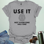 A minimalist graphic design featuring a detailed line-art illustration of a human brain centered between the bold text "USE IT" and "NOT EVERYONE HAS ONE."