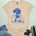 A tan shirt with blue line art illustration of a woman looking frustrated with her head in her hands, above the text 'My social life is like my code:' and 'It needs debugging.