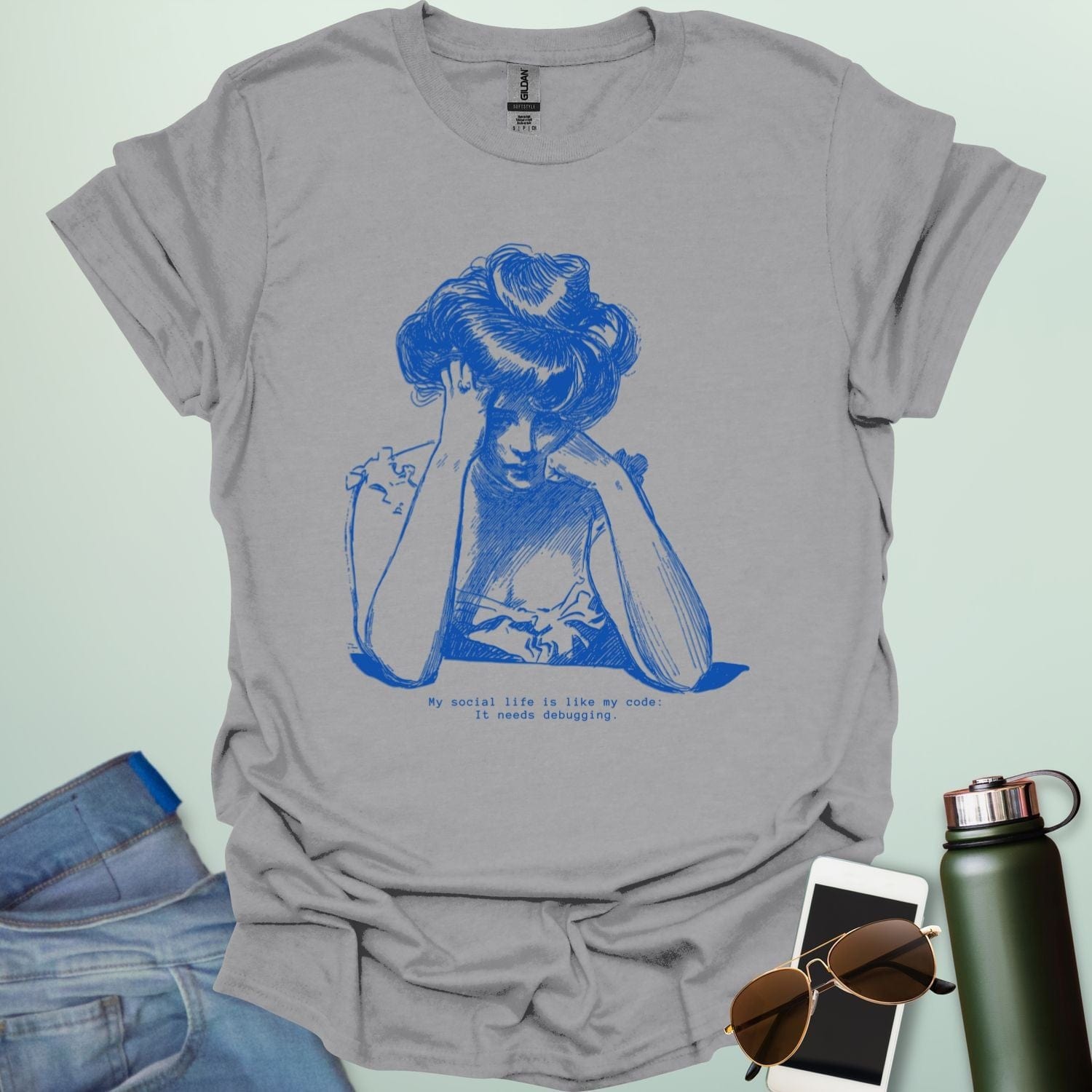 A sport grey shirt with blue line art illustration of a woman looking frustrated with her head in her hands, above the text 'My social life is like my code:' and 'It needs debugging.