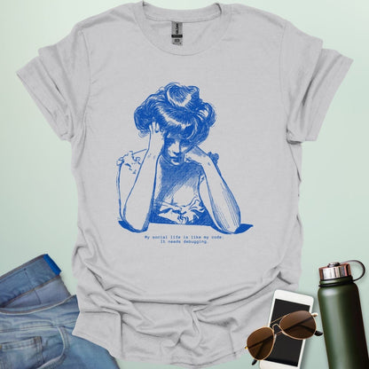 An ice grey shirt with blue line art illustration of a woman looking frustrated with her head in her hands, above the text 'My social life is like my code:' and 'It needs debugging.