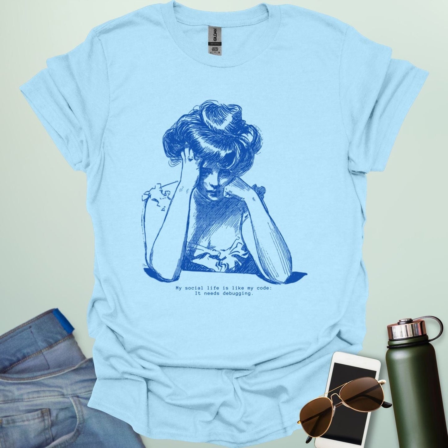 A light blue shirt with blue line art illustration of a woman looking frustrated with her head in her hands, above the text 'My social life is like my code:' and 'It needs debugging.