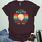 A retro-style graphic featuring the planet Pluto in front of a striped sunset background with the text "PLUTO NEVER FORGET — 1930 - 2006 —".