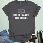 A minimalist graphic design featuring an open book with a red warning triangle and the word "ERROR!" above the bold text "BOOK SMART. LIFE DUMB."