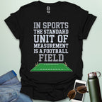 A black t-shirt with the text 'IN SPORTS THE STANDARD UNIT OF MEASUREMENT IS A FOOTBALL FIELD' above an illustration of a football field.