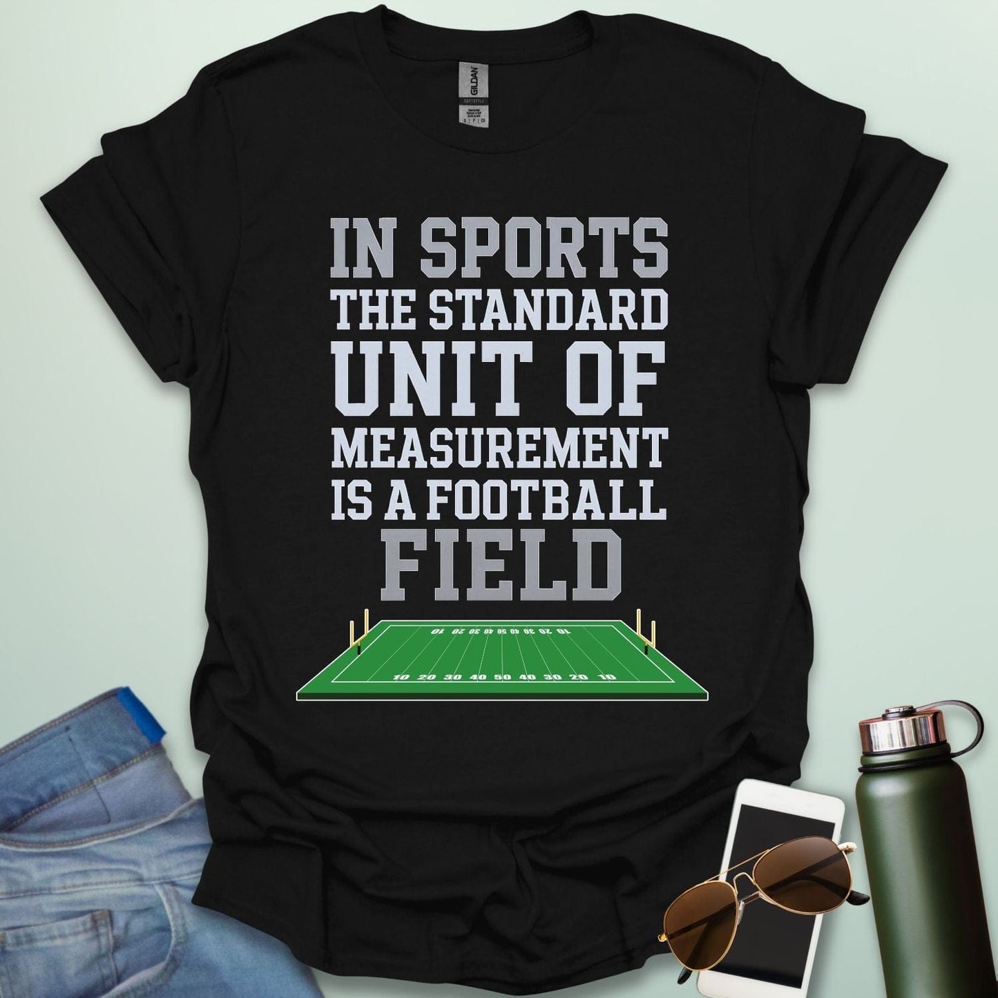 A black t-shirt with the text 'IN SPORTS THE STANDARD UNIT OF MEASUREMENT IS A FOOTBALL FIELD' above an illustration of a football field.