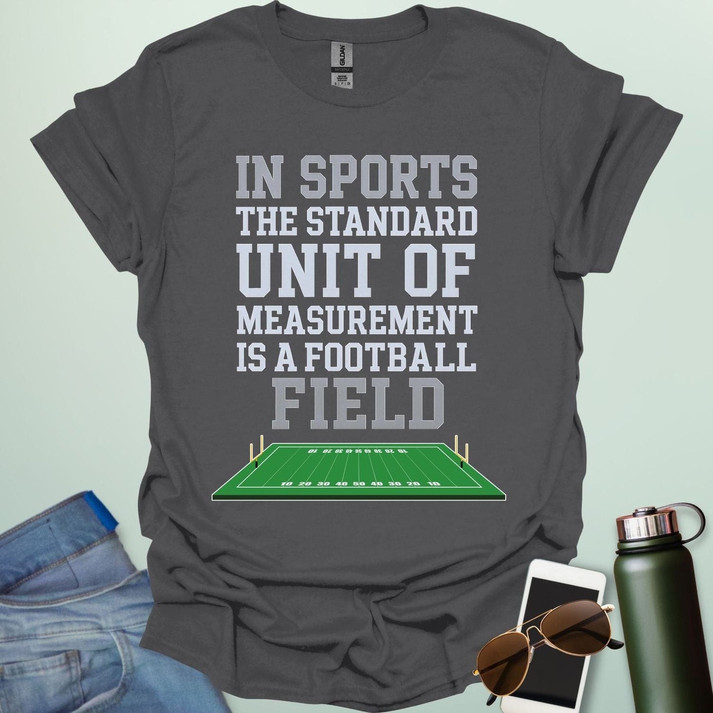 A charcoal grey t-shirt with the text 'IN SPORTS THE STANDARD UNIT OF MEASUREMENT IS A FOOTBALL FIELD' above an illustration of a football field.