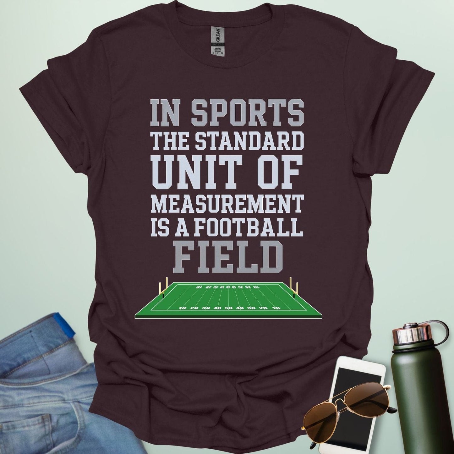 A dark chocolate t-shirt with the text 'IN SPORTS THE STANDARD UNIT OF MEASUREMENT IS A FOOTBALL FIELD' above an illustration of a football field.