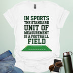 A white t-shirt with the text 'IN SPORTS THE STANDARD UNIT OF MEASUREMENT IS A FOOTBALL FIELD' above an illustration of a football field.