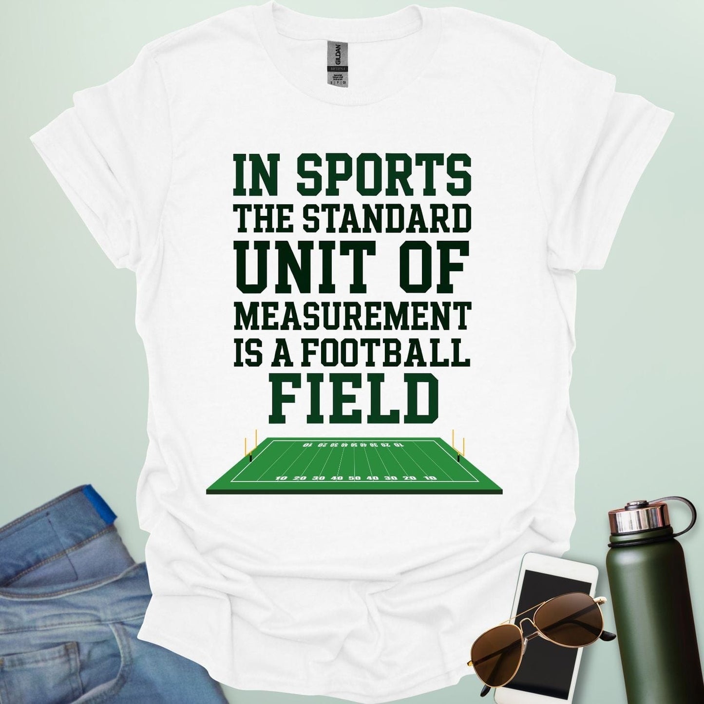 A white t-shirt with the text 'IN SPORTS THE STANDARD UNIT OF MEASUREMENT IS A FOOTBALL FIELD' above an illustration of a football field.