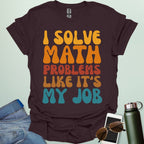 A t-shirt with the text 'I SOLVE MATH PROBLEMS LIKE IT'S MY JOB' printed in a retro, colorful, and bold font.