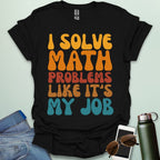 A t-shirt with the text 'I SOLVE MATH PROBLEMS LIKE IT'S MY JOB' printed in a retro, colorful, and bold font.