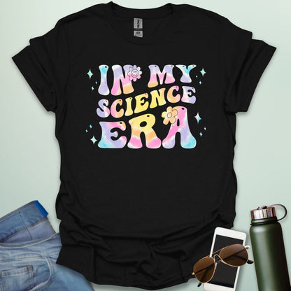 A black t-shirt with wavy, tie-dye text that says 'IN MY SCIENCE ERA' with flowers and stars.
