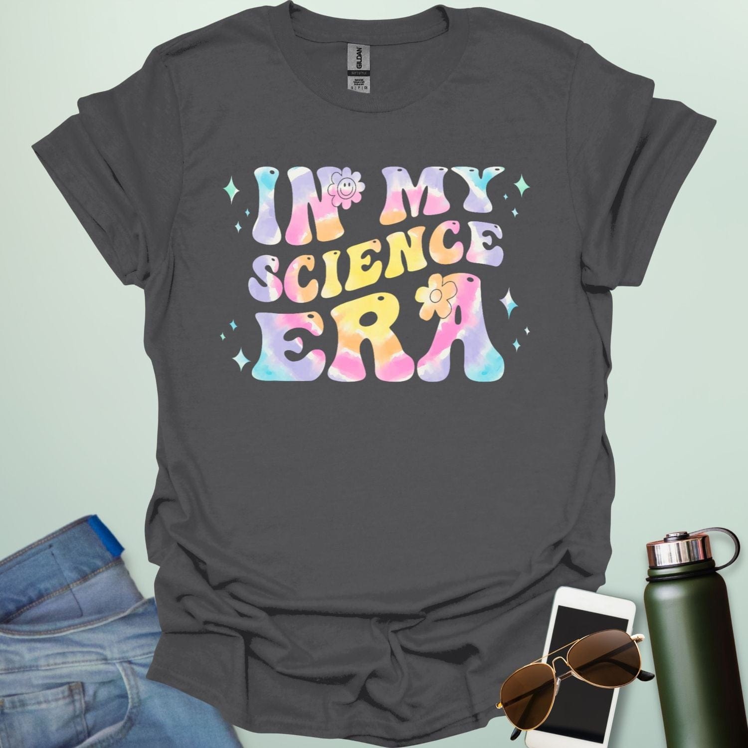 A charcoal grey t-shirt with wavy, tie-dye text that says 'IN MY SCIENCE ERA' with flowers and stars.