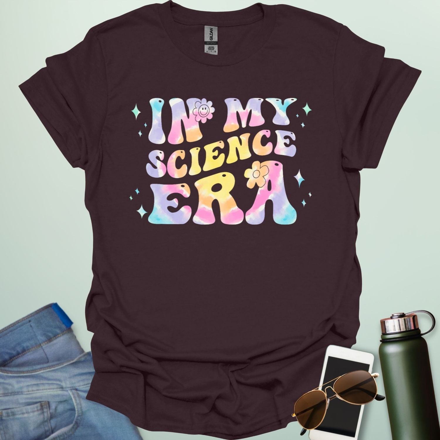 A dark chocolate t-shirt with wavy, tie-dye text that says 'IN MY SCIENCE ERA' with flowers and stars.