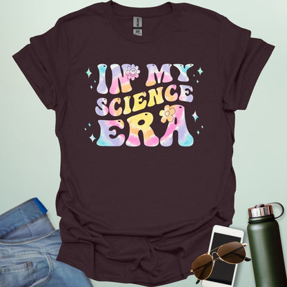 A dark chocolate t-shirt with wavy, tie-dye text that says 'IN MY SCIENCE ERA' with flowers and stars.