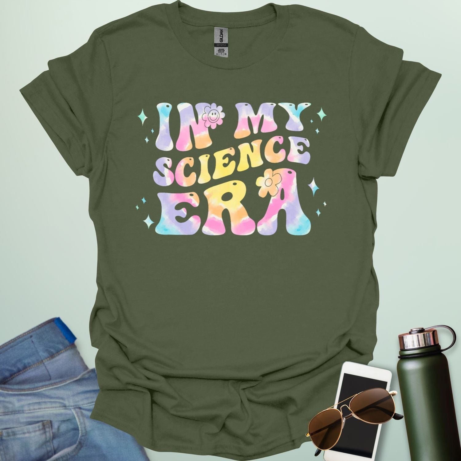 A military green t-shirt with wavy, tie-dye text that says 'IN MY SCIENCE ERA' with flowers and stars.