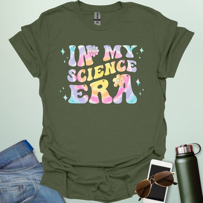A military green t-shirt with wavy, tie-dye text that says 'IN MY SCIENCE ERA' with flowers and stars.