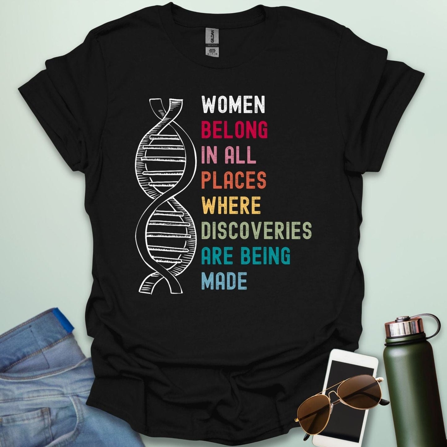 A black t-shirt with the text 'WOMEN BELONG IN ALL PLACES WHERE DISCOVERIES ARE BEING MADE' in a typewriter-style font.