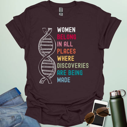 A dark chocolate t-shirt with the text 'WOMEN BELONG IN ALL PLACES WHERE DISCOVERIES ARE BEING MADE' in a typewriter-style font.