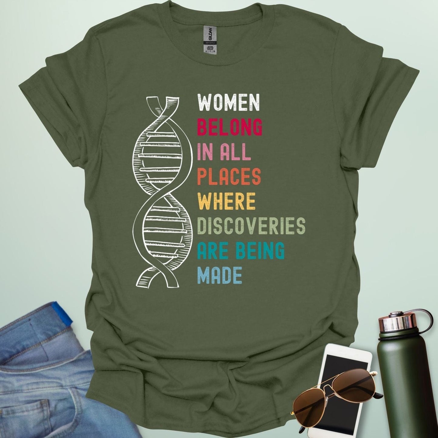 A military green t-shirt with the text 'WOMEN BELONG IN ALL PLACES WHERE DISCOVERIES ARE BEING MADE' in a typewriter-style font.