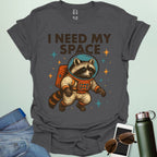 A charcoal grey t-shirt with a cartoon illustration of a raccoon in an astronaut suit and the text 'I NEED MY SPACE.'