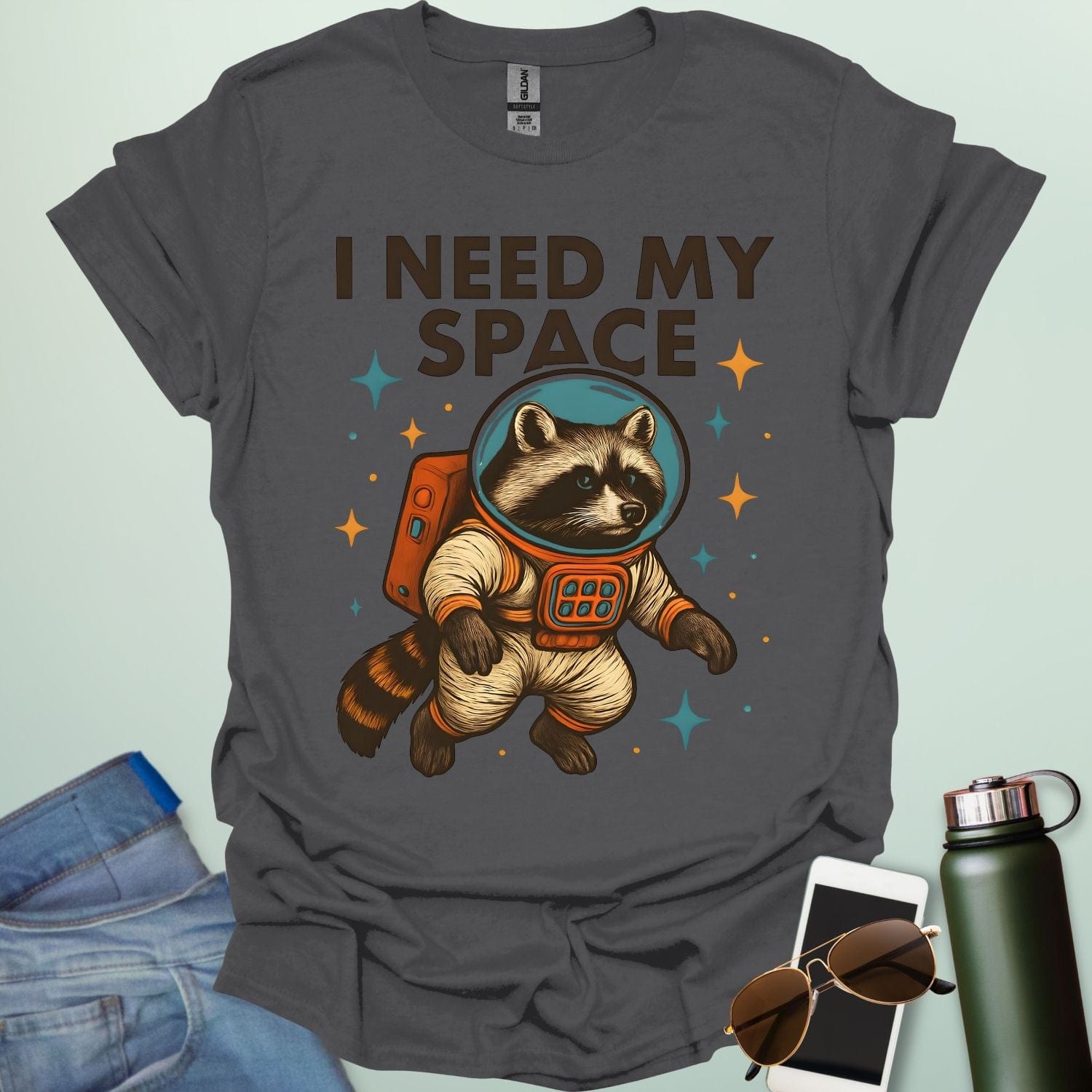 A charcoal grey t-shirt with a cartoon illustration of a raccoon in an astronaut suit and the text 'I NEED MY SPACE.'