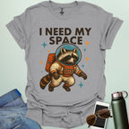 A sport grey t-shirt with a cartoon illustration of a raccoon in an astronaut suit and the text 'I NEED MY SPACE.'
