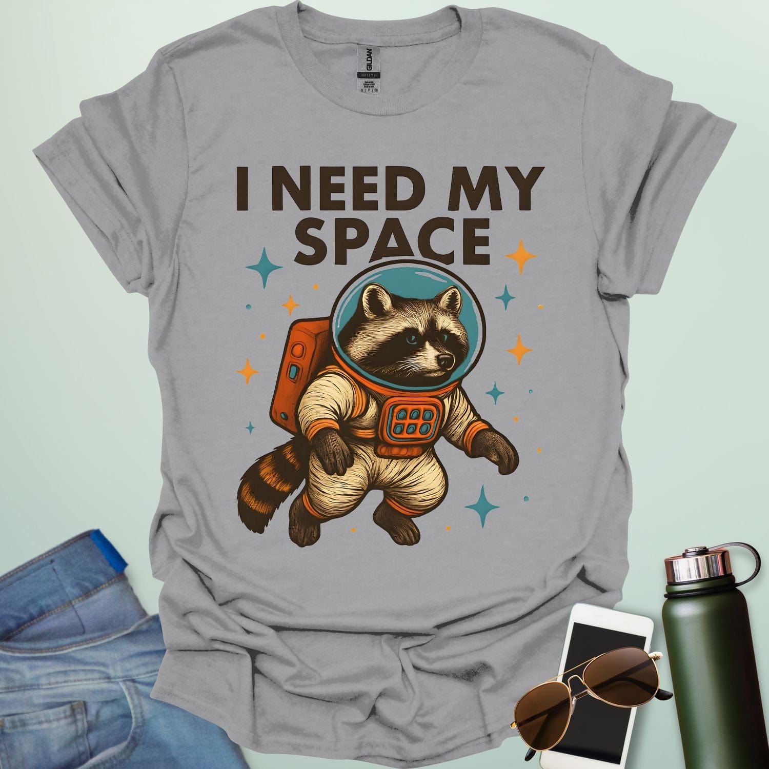 A sport grey t-shirt with a cartoon illustration of a raccoon in an astronaut suit and the text 'I NEED MY SPACE.'