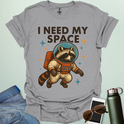 A sport grey t-shirt with a cartoon illustration of a raccoon in an astronaut suit and the text 'I NEED MY SPACE.'