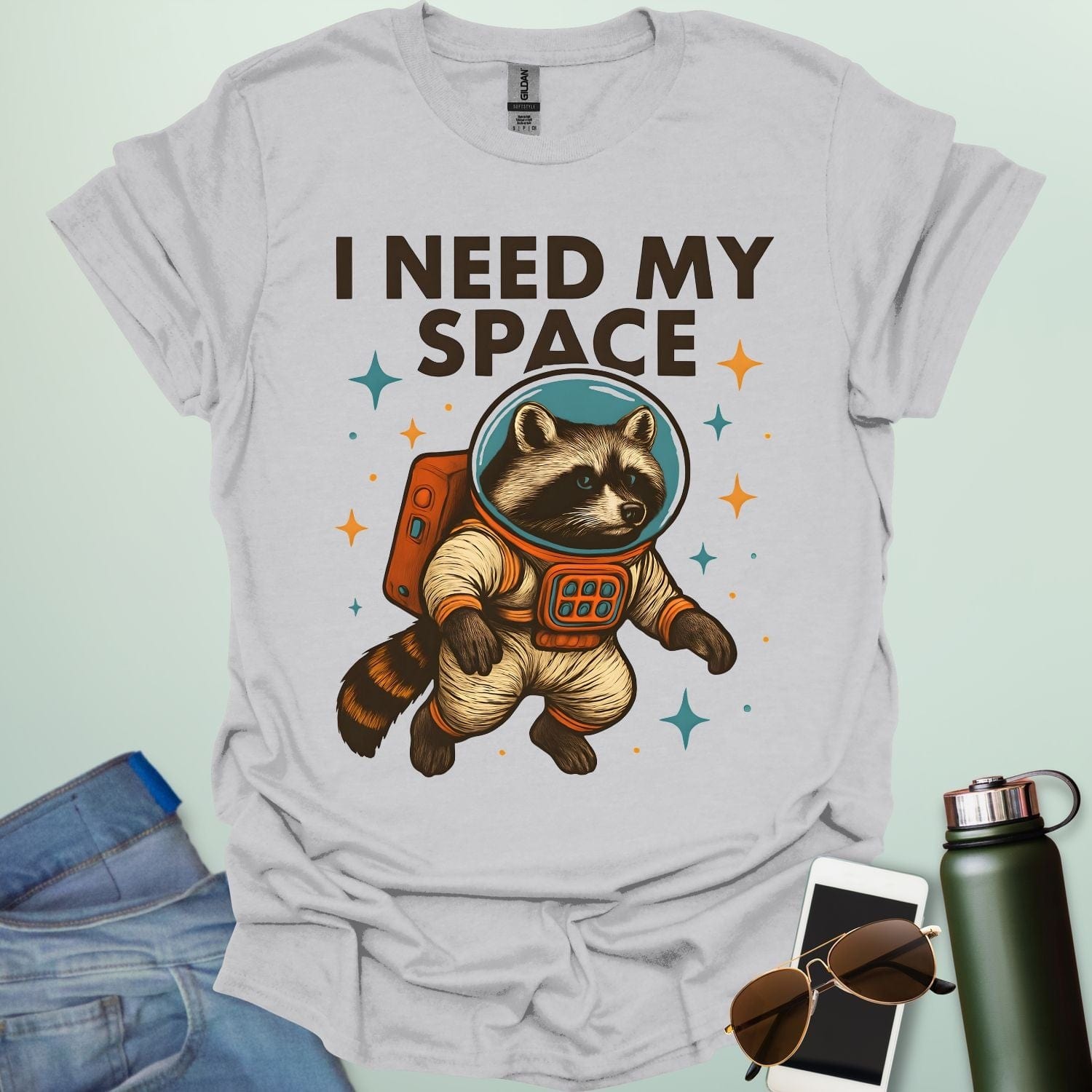 An ice grey t-shirt with a cartoon illustration of a raccoon in an astronaut suit and the text 'I NEED MY SPACE.'