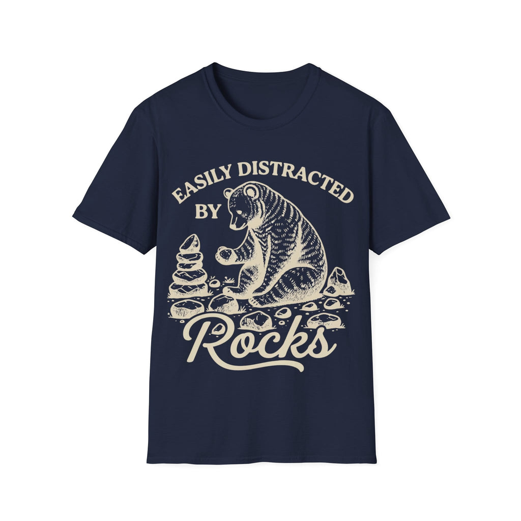 Linocut-style illustration of a bear sitting down examining a stone beside a cairn stack, framed by text reading 'EASILY DISTRACTED BY ROCKS'.