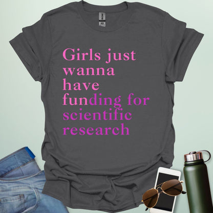 A charcoal grey t-shirt with the text 'Girls just wanna have funding for scientific research' in a pink serif font.