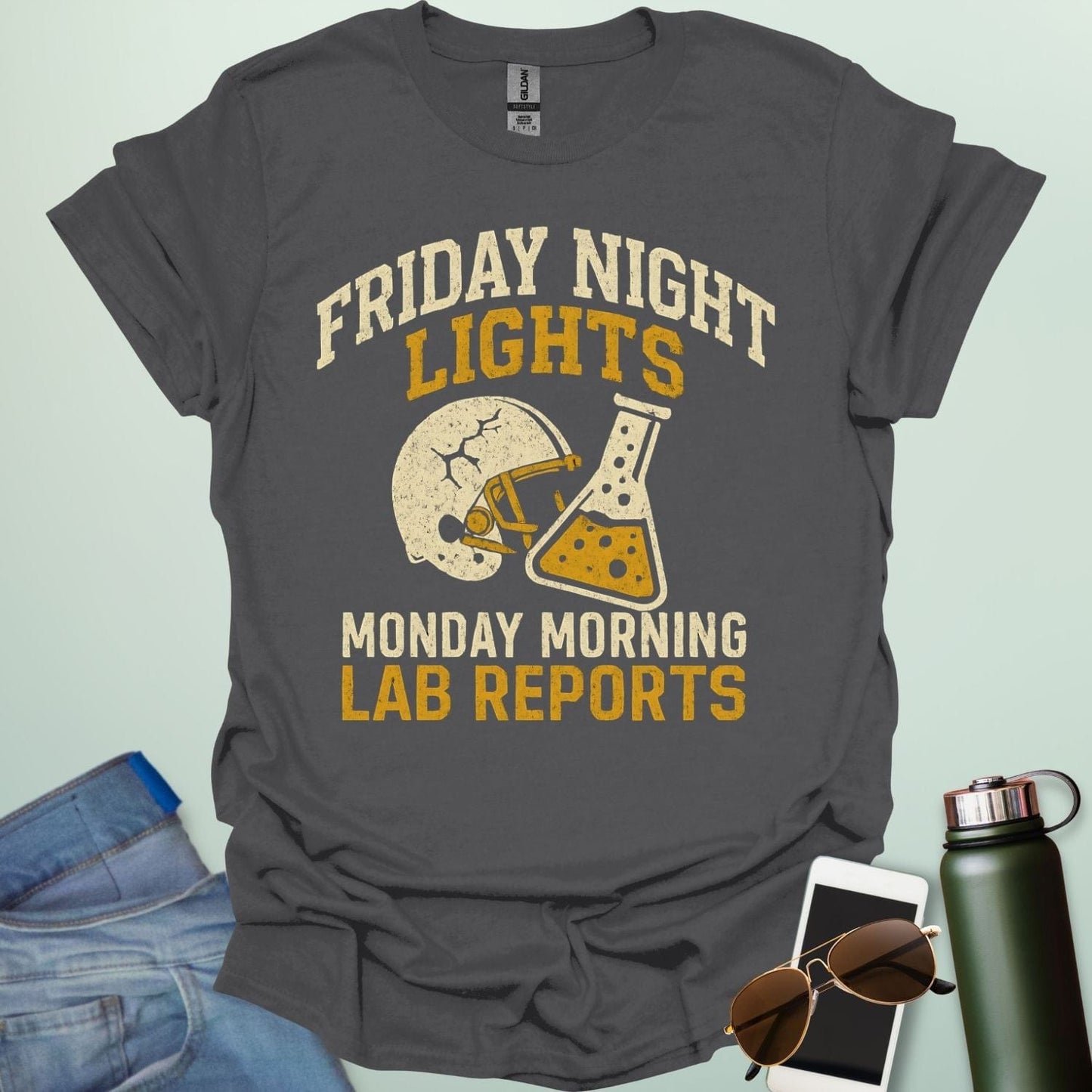 A  charcoal grey t-shirt with a vintage football helmet and a cracked lab flask, with the text 'FRIDAY NIGHT LIGHTS' and 'MONDAY MORNING LAB REPORTS.'
