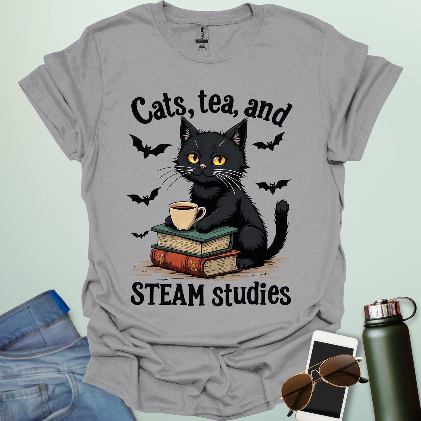 Cats, Tea, and STEAM Studies t-shirt with black cat, books, tea cup, and bats — a cozy geeky design for STEM/STEAM fans and book lovers.
