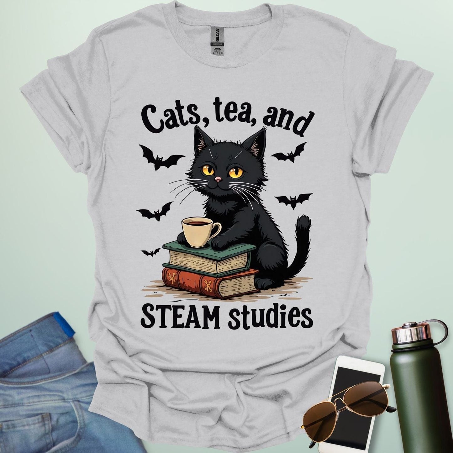 Cats, Tea, and STEAM Studies t-shirt with black cat, books, tea cup, and bats — a cozy geeky design for STEM/STEAM fans and book lovers.